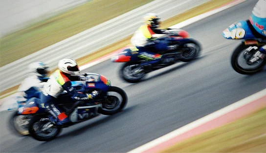 Un groupe de motos de course filant à toute allure sur un circuit, le flou de mouvement soulignant l'intensité de la compétition et le rythme effréné de ce sport automobile.